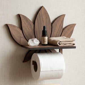 Puede incluir: Un estante de pared de madera marrón oscuro con forma de flor de loto y una superficie horizontal plana. El estante sostiene un pequeño frasco cuentagotas de vidrio con una etiqueta de loto, un cristal de cuarzo transparente y una tela beige.