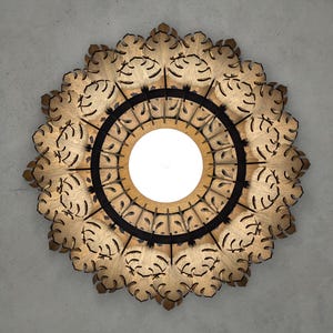 May include: A decorative wooden light fixture with a circular design. The fixture features a central white light source surrounded by a black ring and an outer ring of intricately cut wooden leaves. The overall shape is a symmetrical floral pattern.