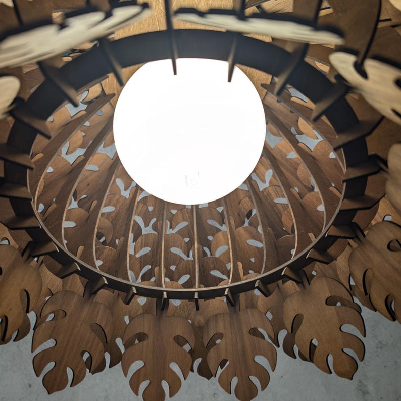 May include: A wooden pendant light fixture with a large, round, white light bulb in the center. The fixture is made of intricately cut wooden pieces in a leaf design. The light fixture is brown and hangs from the ceiling.