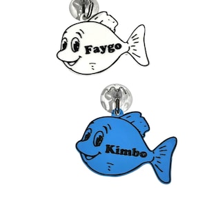 Peut inclure: Deux décorations en forme de poisson de dessin animé. L'un est blanc avec le nom "Faygo" en noir, l'autre bleu avec le nom "Kimbo". Chaque poisson a une ventouse pour l'accrocher.