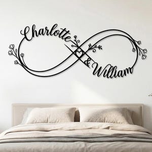 Può includere: Decorazione murale in metallo nero a forma di simbolo dell'infinito con i nomi "Charlotte" e "William" in corsivo. Il simbolo dell'infinito è decorato con elementi floreali e un cuore. L'opera è esposta sopra un letto.