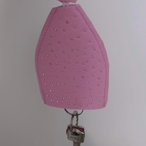 May include: A pink felt keychain with a silver key ring and a set of keys. The keychain is covered in small, sparkly rhinestones.