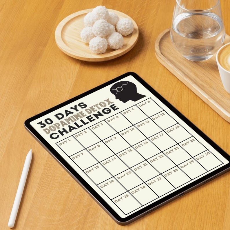 May include: A digital tablet displaying a 30-day dopamine detox challenge calendar. The calendar is divided into 30 squares, each labeled with a day number. The tablet is lying on a wooden surface.