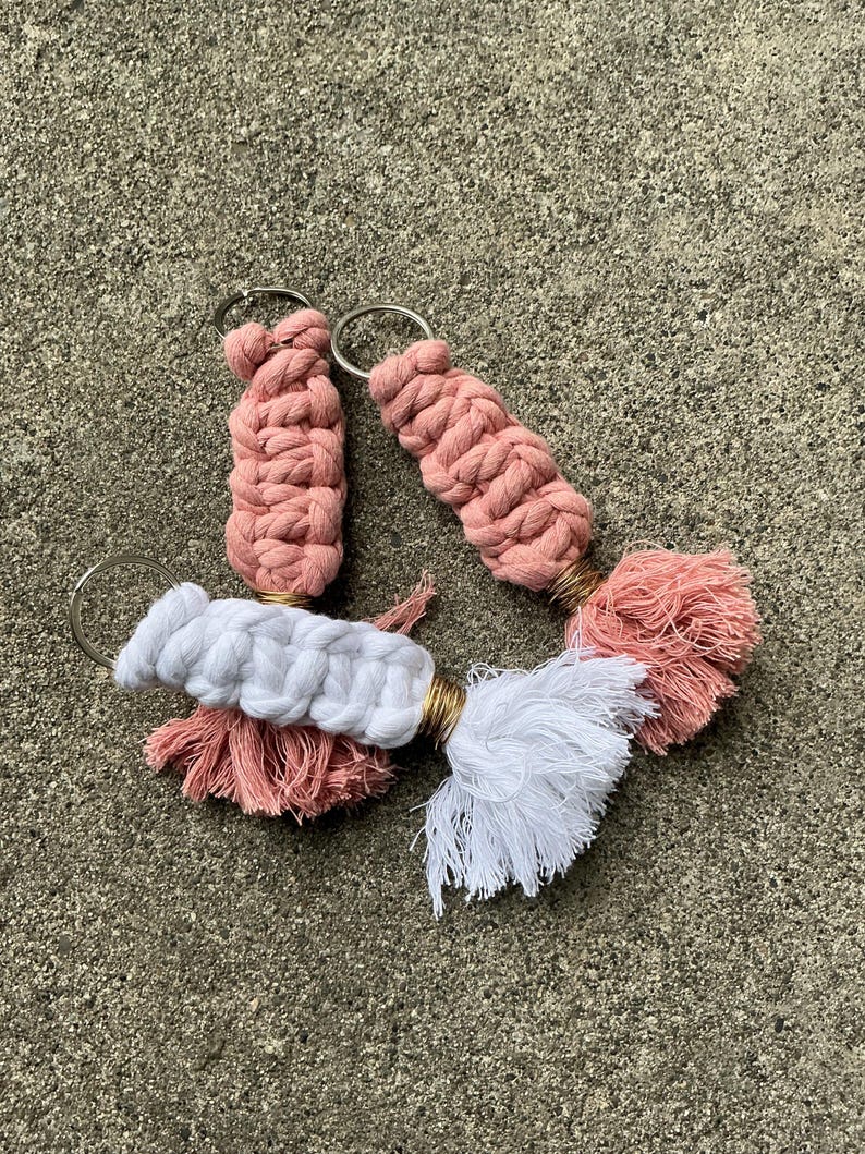K&ouml;nnte beinhalten: Drei rosafarbene und wei&szlig;e geh&auml;kelte Schl&uuml;sselanh&auml;nger mit Quasten. Die Schl&uuml;sselanh&auml;nger sind aus weichem, flauschigem Garn gefertigt und haben ein schlichtes, elegantes Design.