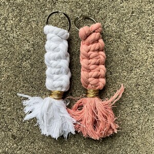 K&ouml;nnte beinhalten: Zwei handgefertigte Makramee-Schl&uuml;sselanh&auml;nger mit Quasten. Einer ist wei&szlig; und der andere ist pfirsichfarben.