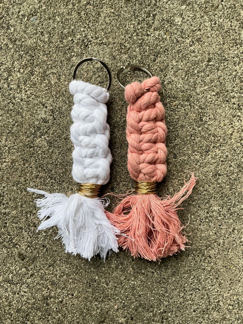 K&ouml;nnte beinhalten: Zwei handgefertigte Makramee-Schl&uuml;sselanh&auml;nger mit Quasten. Einer ist wei&szlig; und der andere ist pfirsichfarben.