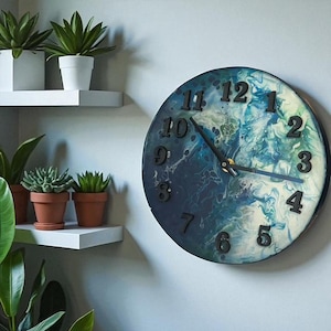 May include: A round wall clock with a blue and white marbled face. Black numerals mark the hours. The clock is mounted on a light gray wall. The image also shows shelves with potted plants.