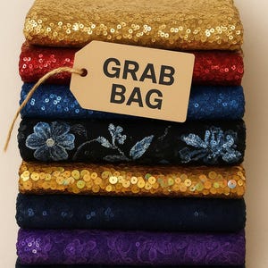 May include: A stack of fabric pieces in various colors, including gold, red, blue, black with floral embroidery, and purple. A tag that says "GRAB BAG" is attached to the stack.