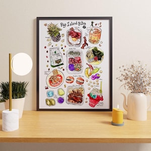 May include: A framed print titled "Big Island Bites" featuring colorful illustrations of various Hawaiian foods. The artwork includes images of pineapple, eggs, cocktails, and other local dishes. The print is displayed on a wooden surface with a lamp, plant, and candle.