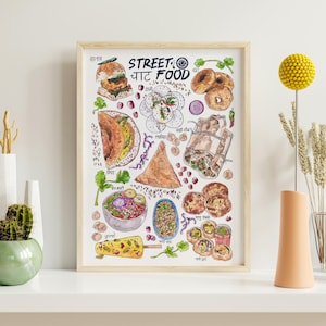 May include: A watercolour illustration of various Indian street foods, including samosas, chaat, and pakoras. The illustration is framed in a light wood frame and has the text "STREET: CHAT FOOD" at the top.