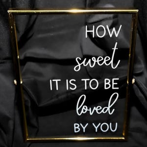 May include: A gold-framed glass sign with the text "How sweet it is to be loved by you" in white lettering.