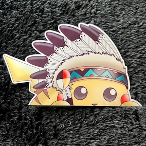 May include: A die-cut sticker featuring a yellow cartoon character wearing a Native American headdress. The headdress is cream-colored with dark purple feathers and a turquoise and brown headband. The character has large brown eyes and red cheeks.