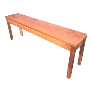 May include: A long, rectangular wooden bench with a reddish-brown finish. The bench has four legs and a simple, clean design. The bench measures approximately 60 inches long.