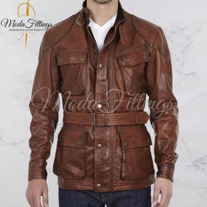 Può includere: Una giacca di pelle marrone con cintura, quattro tasche e chiusura con bottoni. La giacca ha un colletto e maniche lunghe.