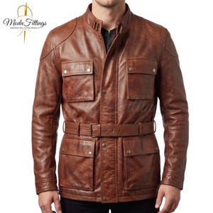 May include: A brown leather jacket featuring a stand-up collar with a buckle strap, a front button closure, and four large flap pockets on the chest and waist. The jacket includes a matching leather belt at the waist and long sleeves with cuffs.