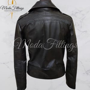 May include: Black leather jacket with a zipper closure and a collar. The jacket has a quilted design on the back and a logo that says "Moda Fittings Handmade Real Leather Products".