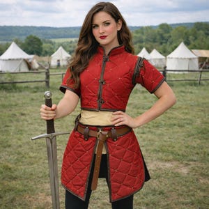 May include: A red quilted medieval-style outfit with brown trim and a matching belt. The outfit includes a short-sleeved top and a skirt-like bottom. A long sword is held in the hand.