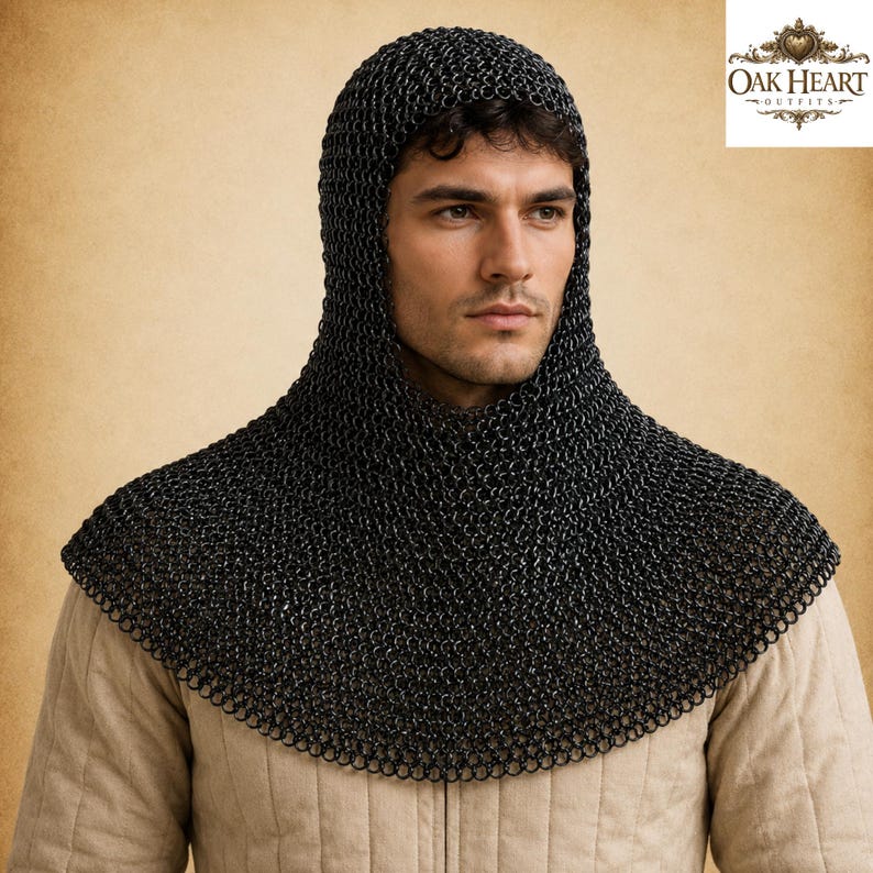 May include: Black chainmail coif with a hood, designed to protect the head and neck. The coif is made of small, interlocking metal rings. The image also includes the Oak Heart Outfits logo in the upper right corner.