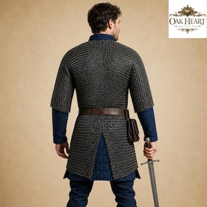 May include: A medieval chainmail shirt with short sleeves, worn over a blue tunic. A brown leather belt and pouch are visible. The person is holding a sword. The Oak Heart Outfits logo is in the upper right corner.