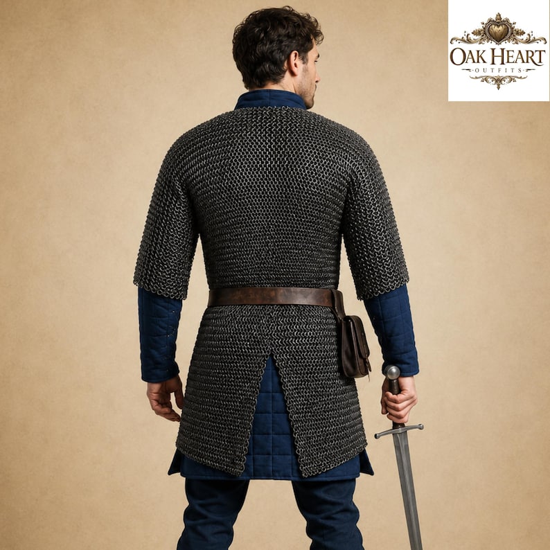 May include: A medieval chainmail shirt with short sleeves, worn over a blue tunic. A brown leather belt and pouch are visible. The person is holding a sword. The Oak Heart Outfits logo is in the upper right corner.