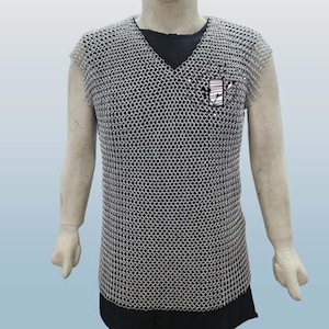 May include: A sleeveless chainmail shirt with a V-neck design. The shirt is made of small, interlocking metal rings, creating a flexible, protective garment. A small patch is visible on the chest. The shirt is worn over a black undershirt.