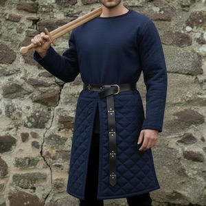 May include: A navy blue quilted tunic with a long-sleeved top and a black leather belt. The tunic features a diamond pattern and a split front. A wooden sword rests on the shoulder. The outfit is suitable for historical reenactments or costume events.
