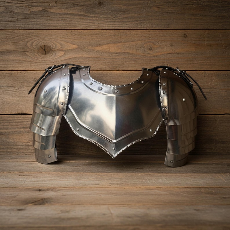 Pode incluir: Um peitoral e ombreiras prateados e polidos. A armadura de metal apresenta uma constru&ccedil;&atilde;o rebitada e pe&ccedil;as de ombro articuladas. A armadura de estilo medieval &eacute; exibida em uma superf&iacute;cie de madeira.
