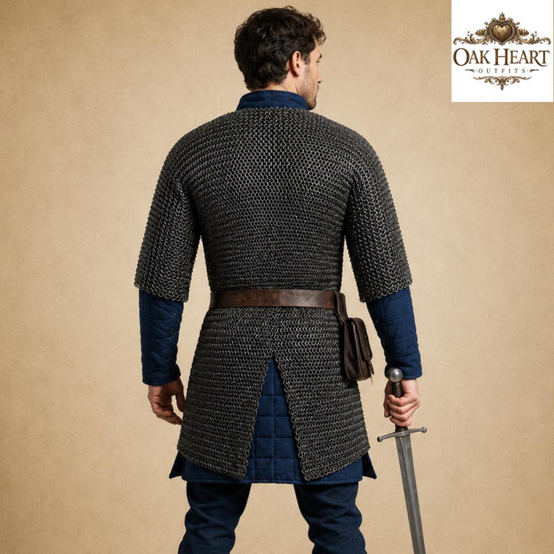 May include: A medieval chainmail shirt with short sleeves, worn over a blue tunic. A brown leather belt and pouch are visible. The person is holding a sword. The Oak Heart Outfits logo is in the upper right corner.