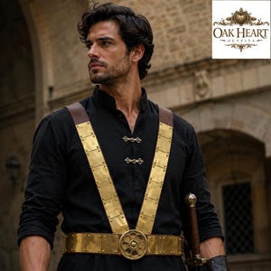 Puede incluir: Una camisa negra de manga larga con cuello mao y dos cierres metálicos plateados. Sobre la camisa, un arnés de cuero marrón con filas verticales de placas rectangulares de latón y una hebilla central circular de latón con detalle floral.
