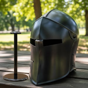 May include: A black medieval helmet with a visor and a chain detail, displayed on a black stand. The helmet is made of metal and has a smooth, reflective surface. The stand is round at the base and top, with a straight, black pole.