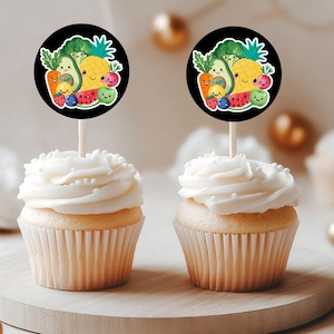 Puede incluir: Dos cupcakes con glaseado blanco y chispas, coronados con adornos redondos para cupcakes en blanco y negro que muestran una ilustración de dibujos animados de varias frutas y verduras con caras sonrientes.