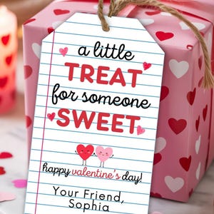 May include: A gift tag with the message "a little TREAT for someone SWEET" in red and black lettering, with heart illustrations. The tag is attached to a pink gift box with a matching bow and hearts. The tag also says "Happy Valentine's Day!" and "Your Friend, Sophia."