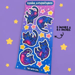 K&ouml;nnte beinhalten: Ein Stickerbogen mit f&uuml;nf Cartoon-Katzen mit Galaxie-Design, umgeben von rosa und gelben Sternen. Der Text "COSMIC CATVENTURES" und "ART WITH CHO" befinden sich oben und unten. Der Bogen misst 7,6 cm x 16,5 cm.