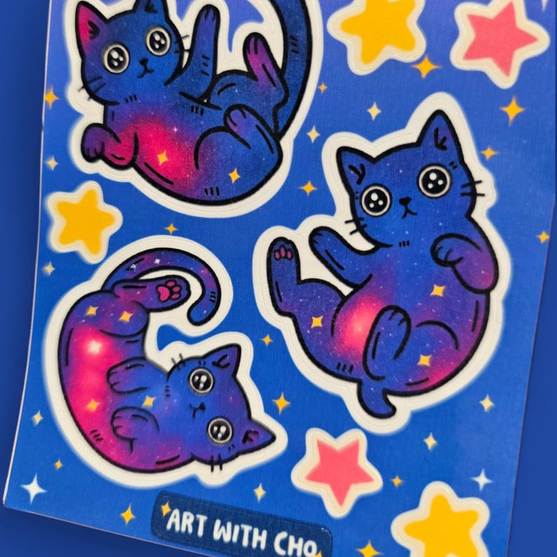K&ouml;nnte beinhalten: Bogen mit Aufklebern mit Cartoon-Katzen im Galaxie-Design in Blau-, Lila- und Rosat&ouml;nen. Die Katzen sind von gelben und rosa Sternen umgeben. Der Text "ART WITH CHO" befindet sich unten.