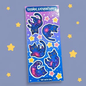 K&ouml;nnte beinhalten: Ein Stickerbogen mit sechs blauen Katzenillustrationen mit einem kosmischen Galaxien-Design. Die Katzen befinden sich in verschiedenen spielerischen Posen, umgeben von rosa und gelben Sternen. Der Text "Cosmic Catventures" und "Art with Cho" befindet sich oben und unten.