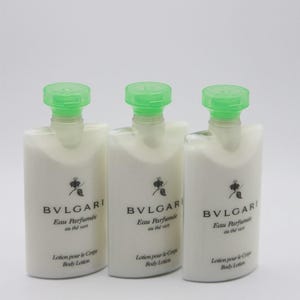 May include: Three white body lotion bottles with green caps. The bottles are labeled "BVLGARI Eau Parfumée au thé vert" and "Lotion pour le Corp Body Lotion". The bottles are rectangular with rounded tops.