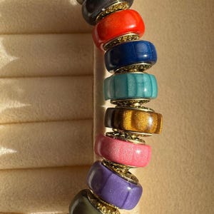 Peut inclure: Un bracelet coloré avec une bande en métal doré et des perles cylindriques. Les perles sont de différentes couleurs, dont le rouge, le bleu, le vert et le violet, avec des détails dorés. Un accessoire de mode.