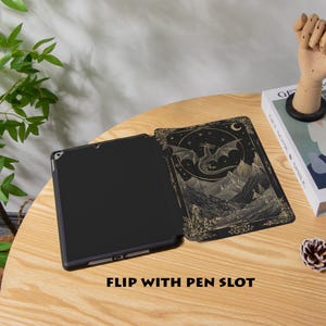 May include: Black tablet case with a dragon and mountain design. The case is open, revealing the tablet screen. The cover features a detailed illustration in gold and black, with the text "FLIP WITH PEN SLOT" at the bottom.