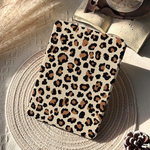 May include: A rectangular case with a beige background and a leopard print pattern in black and brown. The case is placed on a beige woven placemat. The words "Glow Dwell Designs" are printed on the bottom left.