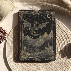 Puede incluir: Funda rectangular negra con una ilustración de dragón dorado, montañas y una luna creciente. La funda tiene un borde dorado decorativo y el texto "Glow Dwell Designs". El diseño está sobre un fondo negro.