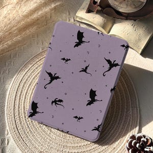 May include: A rectangular e-reader case in a light purple color featuring a repeating pattern of black silhouettes of flying dragons, small stars, and crescent moons. The text Glow Dwell Designs is printed in the bottom left corner.