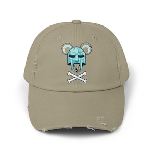 Op de afbeelding: Een beige, verweerde baseballpet met een blauwe en witte cartoonmuis die een helm draagt en gekruiste botten vasthoudt.