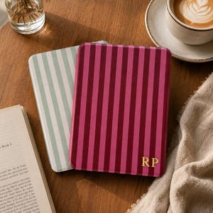 May include: Two rectangular e-reader cases with rounded corners. The top case features vertical stripes in two shades of magenta and pink with the gold-colored initials RP in the bottom right corner. The bottom case has light green and white stripes.