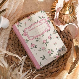 Könnte beinhalten: Eine Hülle mit floralem Muster aus rosa Rosen und grünen Blättern, mit dem Text "COMPOSITION BOOK". Die Hülle hat einen rosa Rand und den Text "Personalisieren Sie Ihre Hülle mit Ihrem Namen". Der Name "Sophia" wird in Schriftart #1 angezeigt.