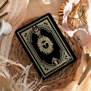 Könnte beinhalten: Eine schwarze Handyhülle mit goldenen, verzierten Details, mit einem zentralen Emblem und dekorativem Rand. Die Hülle wird auf einer gewebten Matte mit dem Text "Personalisiere deine Hülle mit deinem Namen." und "Sophia - Font #1." präsentiert.
