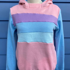 May include: A light blue hooded sweatshirt with horizontal stripes in pink, purple, and light blue.