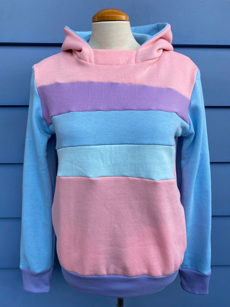May include: A light blue hooded sweatshirt with horizontal stripes in pink, purple, and light blue.