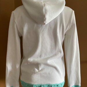 May include: White hooded sweatshirt with a light blue trim around the hood, cuffs, and hem.