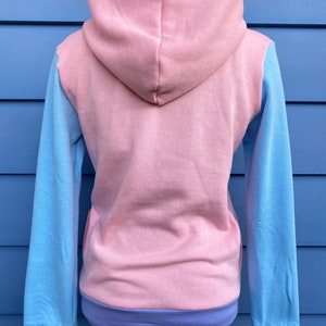 May include: A pink hooded sweatshirt with blue sleeves and a purple trim. The sweatshirt is made of a soft, comfortable fabric and has a relaxed fit.