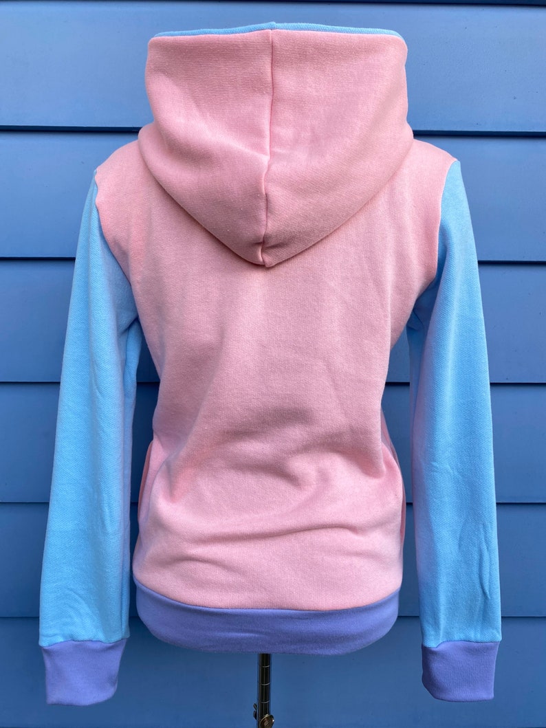 May include: A pink hooded sweatshirt with blue sleeves and a purple trim. The sweatshirt is made of a soft, comfortable fabric and has a relaxed fit.